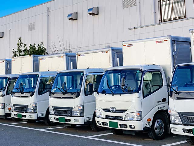 Several white delivery trucks parked in a row beside a building with a light gray exterior.