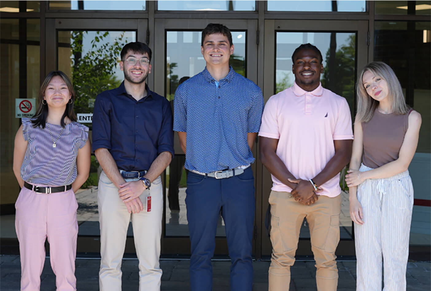 Five people in casual attire stand in front of a building, smiling at the camera.